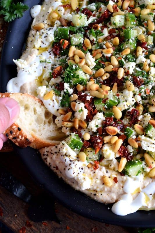 What's a party without dip? Hummus Party Dip Platter is a large, layered dip that's just perfect for entertaining a crowd. This all-in-one dip has hummus, sour cream, pine nuts, sun dried tomatoes, cucumbers, feta, and a few other ingredients too! Serve this on any occasion for a delicious, crowd-pleasing appetizer! #hummus #dip #appetizer #party #platter #spread