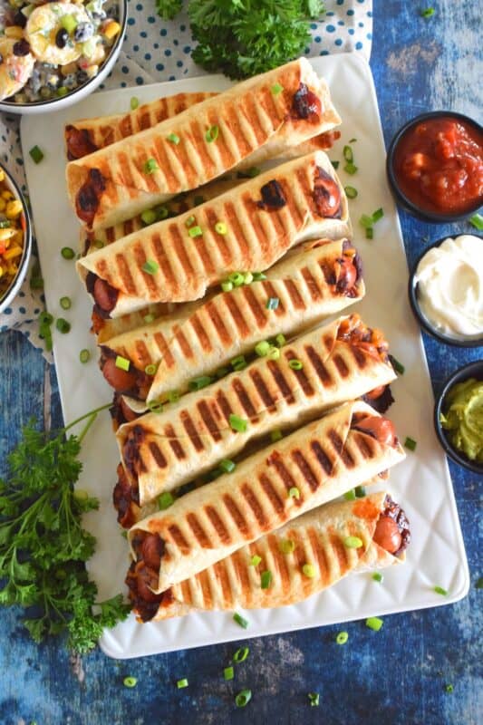 If you cannot decide whether you want a hot dog, a burrito, or a taquito for dinner, then you should just have all three in one! Bean and Cheese Hotdog Taquitos are prepared by rolling a tortilla with refried black beans, shredded cheese, and a hotdog. Grill until golden and crispy. Serve with your favourite dippers! #bbq #bean #cheese #hotdog #taquitos