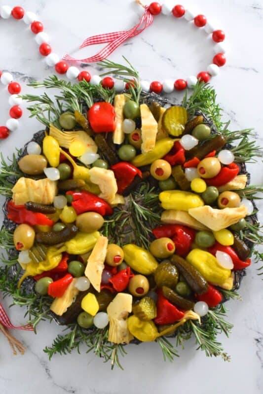 This bright and shiny edible wreath is packed full of sweet, salty, and tangy flavour! Consisting of your favourite pickled and marinated foods, an Olive and Pickle Wreath is the answer to every host's holiday appetizer table. Assemble on a platter and refrigerate until ready to serve. It's easy, delicious, and festive! #olives #pickles #charcuterie #christmas #holiday #partyfood