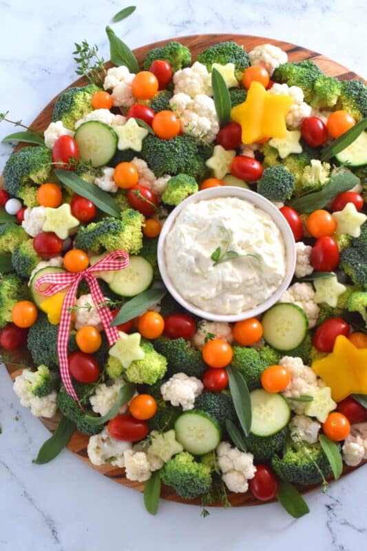 Every party needs a platter or two of finger foods for everyone to munch on. No matter what type of party you're hosting, it most certainly needs a Holiday Vegetable Wreath platter. This gorgeous wreath is prepared using fresh broccoli, cauliflower, tomatoes, cucumbers, and more! Serve with your favourite vegetable dip! #christmas #holiday #partyfood #appetizers #veggieplatter #veggies