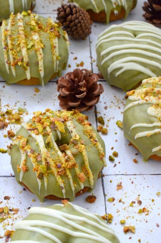 Everything is coming up green in these Matcha Pistachio Donuts!  The batter is light and fluffy and prepared with finely chopped pistachios and matcha.  Dipped in matcha-infused icing and drizzled with white chocolate, these donuts are delicious and addictive! #matcha #greentea #donuts #pistachio