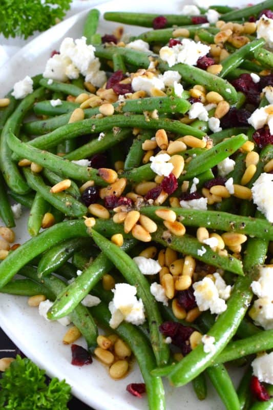 This delicious side dish prepared with green beans, toasted pine nuts, crumbled goat cheese, and dried cranberries takes only fifteen minutes in a skillet on your stovetop! How's that for a quick and easy holiday side?  Perfectly seasoned and quickly sauteed in butter, these green beans are delectably savoury! #greenbeans #cheese #pinenuts #thanksgiving #side